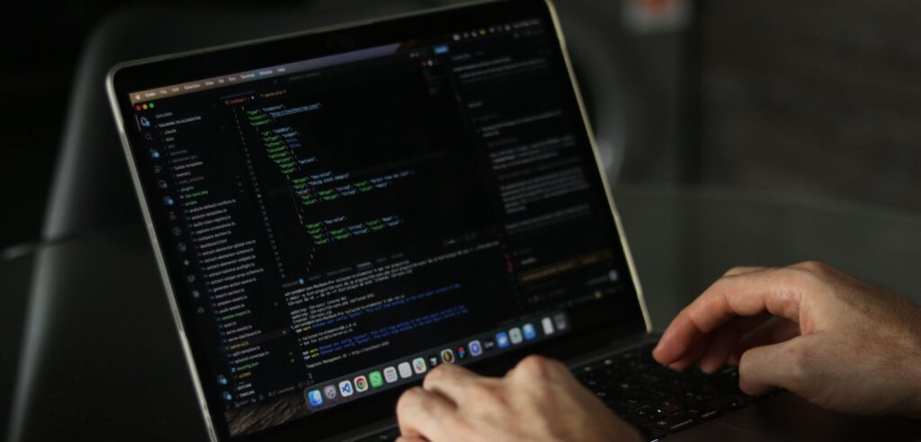 Close-up of hands coding on a laptop, hacking into supply chain software.